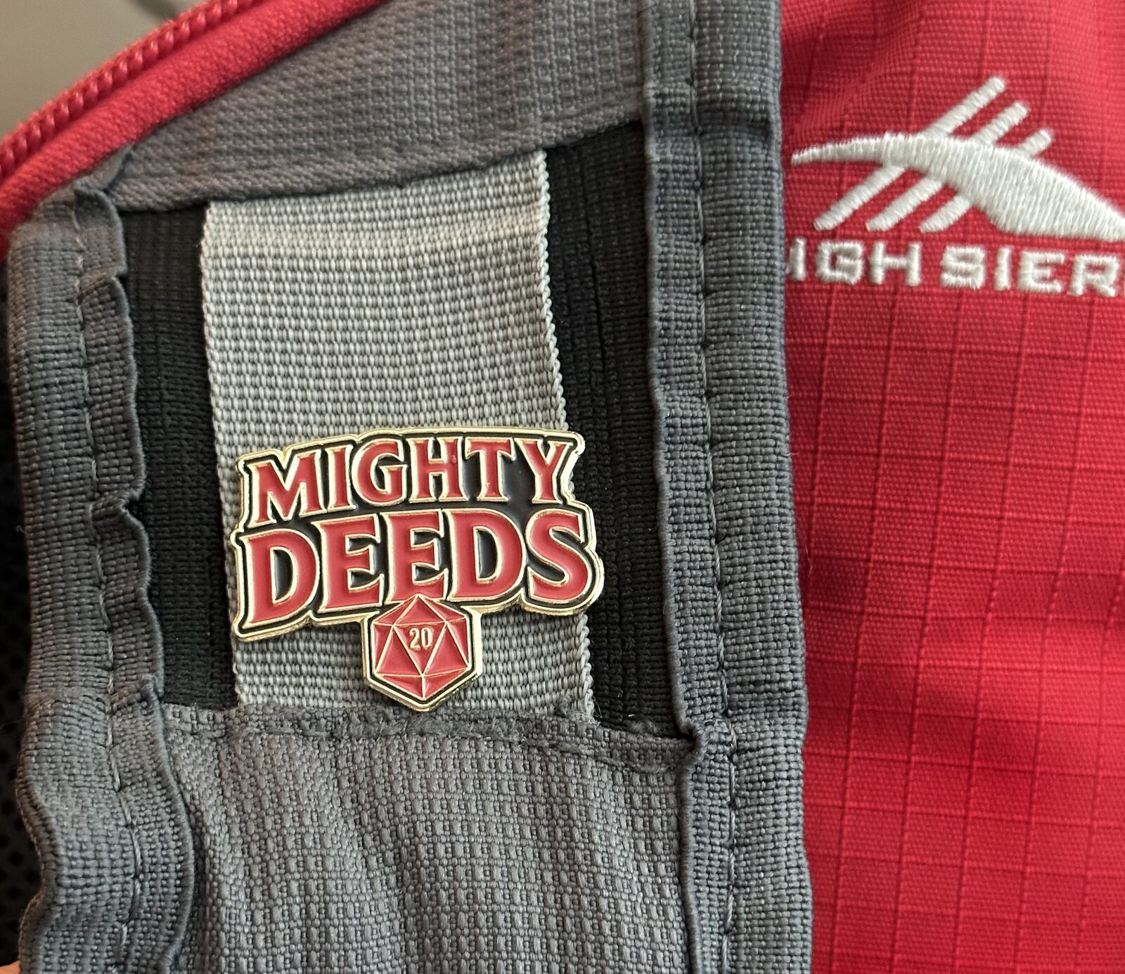 Mighty Deeds enamel pin attached to a backpack strap