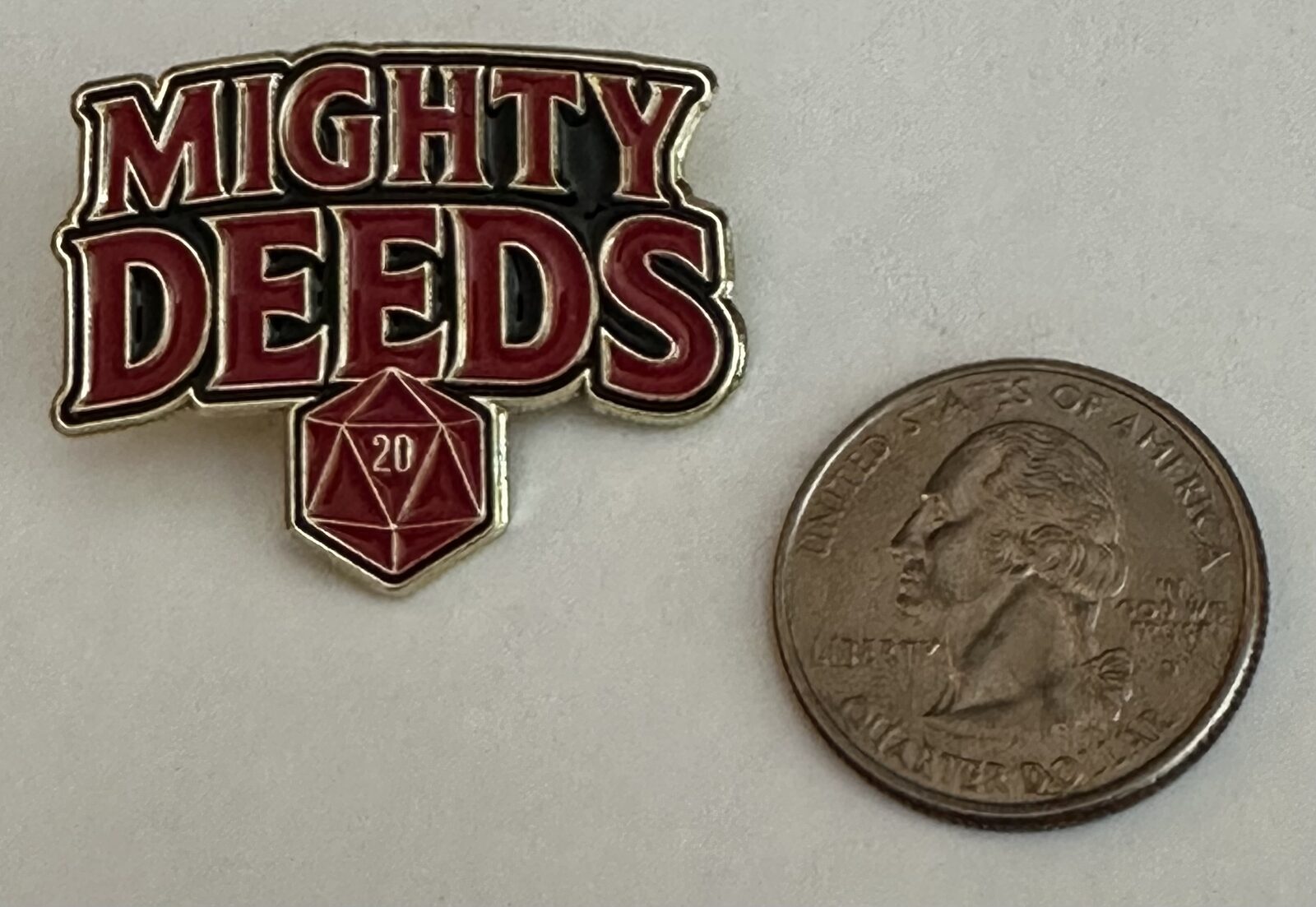 Mighty Deeds enamel pin next to a quarter for size comparison